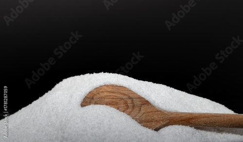Iodated salt pile is poured out in front of black background with wooden spoon. Textured horizontal photo, closeup. V31