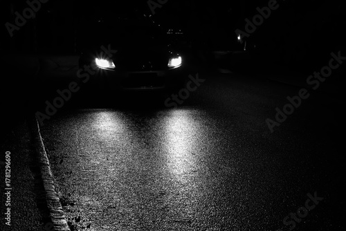 Black car with headlights driving on wet asphalt in the night.