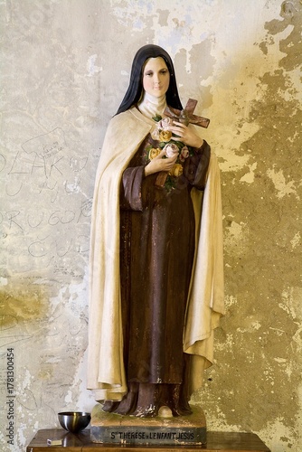 Old statue of Saint Therese of Lisieux against a weathered wall