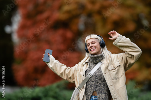 Young woman enjoying music, dancing with headphones outdoors