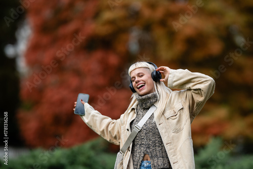 Young woman enjoying music and dancing in autumn park