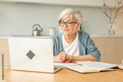Online education courses webinar concept. Middle aged senior woman using laptop computer writing notes. Focused mature old woman enjoying studying online from home written records doing online work