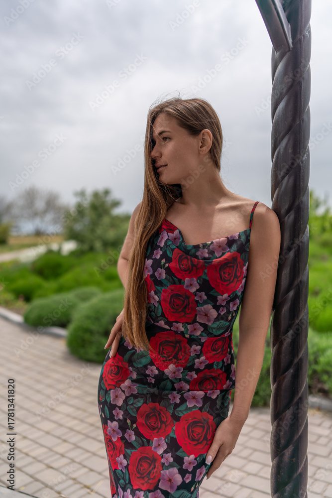 Naklejka premium Woman floral dress park. Beautiful young woman in summer dress leaning against column looking away