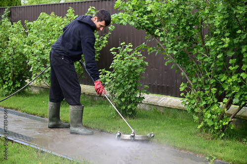 Man cleaning outdoor pathway with pressure washer in a garden during the day