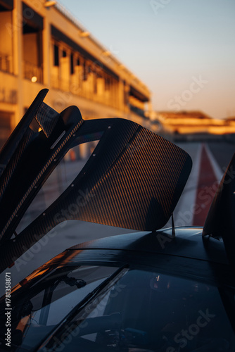 Carbon supercar on the pitlane with open falcon wings style doors at the sunset