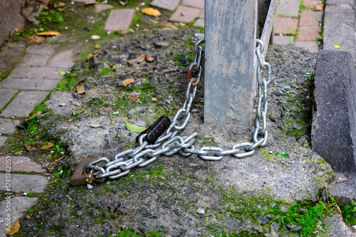 A chain is tied to a metal pole. The chain is locked and the lock is missing. The chain is on a brick walkway