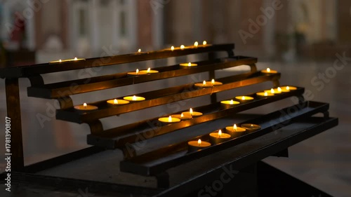 Votive candles burning in a church creating a spiritual atmosphere. Many small votive candles burning brightly on a tiered metal stand inside a dimly lit church, creating a spiritual atmosphere