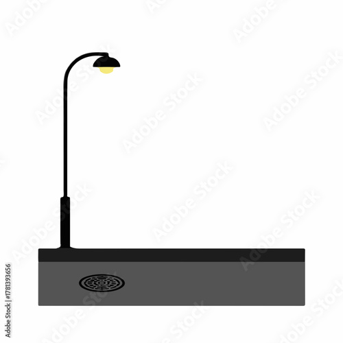 Urban street scene with street lamp illuminating pavement and drainage cover. Urban street elements include functional lamp and clean sidewalk contrasting against blank background.
