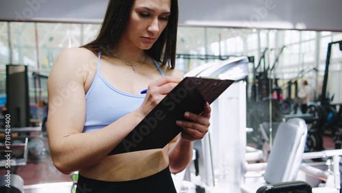 Free Download Fitness trainer documenting workout plan in modern gym during afternoon session - GFXLoad