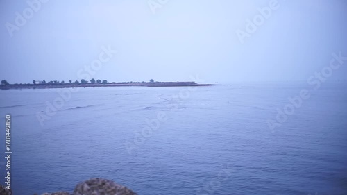 A serene coastal scene featuring the ocean meeting the horizon under a hazy, overcast sky.