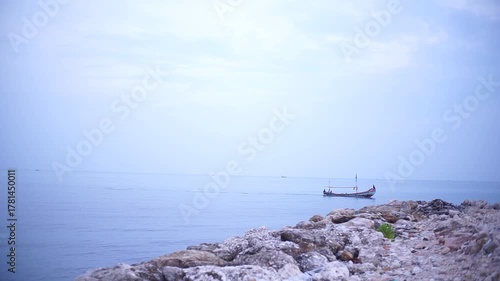 A serene seascape featuring a small boat sailing on the calm, vast ocean under a pale sky.