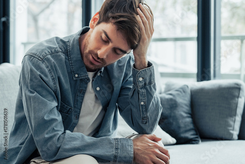 Fotografia Tired Caucasian young man sit on couch touch massage head suffer from headache o