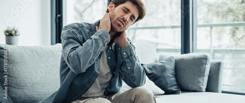 Upset tired young man feeling pain massaging stiff neck rubbing tensed muscles to relieve back ache joint shoulder discomfort after long sedentary work in incorrect posture, fibromyalgia concept