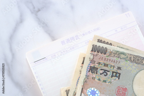預金通帳と1万円札 - テーブルの上に開いた状態で置かれた銀行の預金通帳と、1万円札
