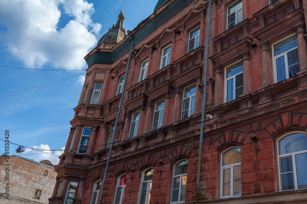 Fototapeta premium Tall historic red brick building with decorative roof under blue sky