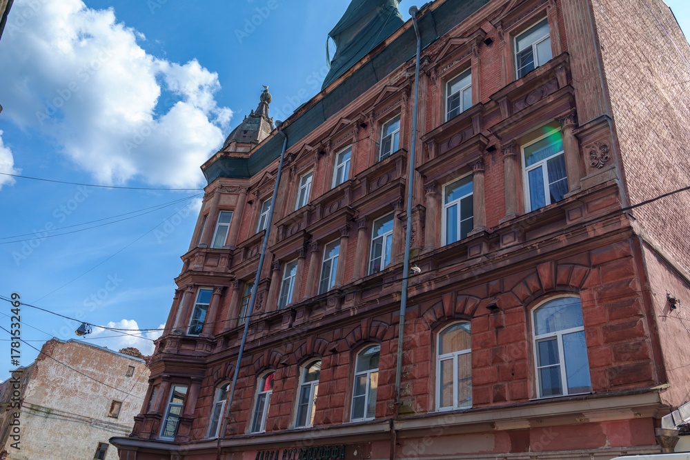 Fototapeta premium Tall historic red brick building with decorative roof under blue sky