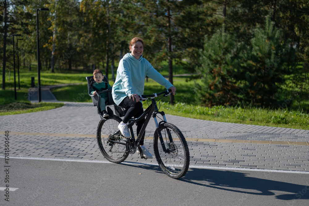 Fototapeta premium Caucasian woman rides bicycle with one-year-old son in park. 