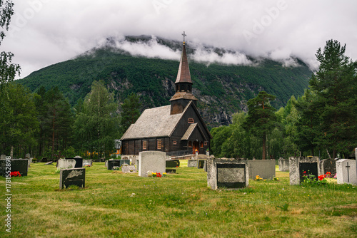 Gjøra Chapel stands in a serene graveyard with gravestones, framed by a cloudy mountain backdrop in Sunndal Municipality, Møre og Romsdal, Norway