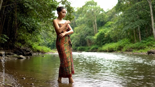 Young Woman in Traditional Attire Standing in a Serene Jungle River.