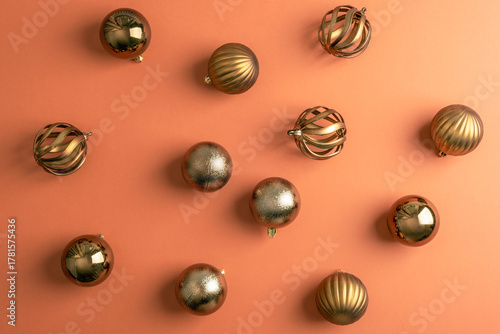 Golden Christmas baubles arranged on warm orange background. Pattern, top view