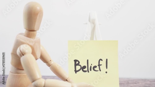 A wooden figure sits on a table with a yellow sign that says 