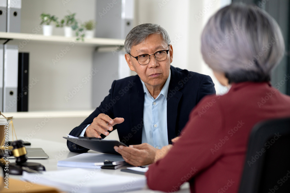 Fototapeta premium Asian senior legal professional discusses important documents with client at office consultation session offering expert advice