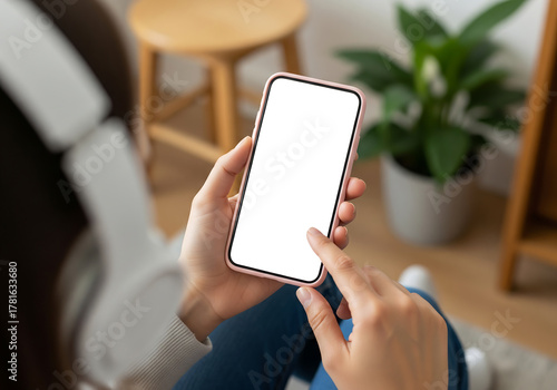 Person Holding Pink Smartphone with White Screen in Cozy Room with Wooden Stool Plant Cabinet and Headphones on Floor