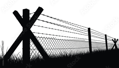 Silhouette of a barbed wire fence with concrete barriers and grass in the foreground
