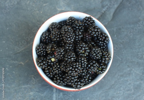 Sweet ripe blackberries, lat. Rubus fruticosus Thornless in a red bowl. Detail of a bowl full of ripe blackberries on the stone table. Flat lay.
