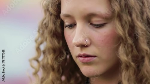Young woman with curly hair looks down with thoughtful expression, colorful background, suitable for emotion