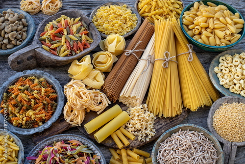Different types of Italian pasta on rustic wooden table, in the spoons, cutting board and bowls 