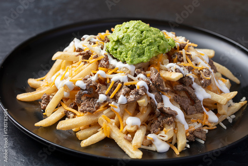 Carne asada with fries, guacamole, cream and melted cheese on a black plate 