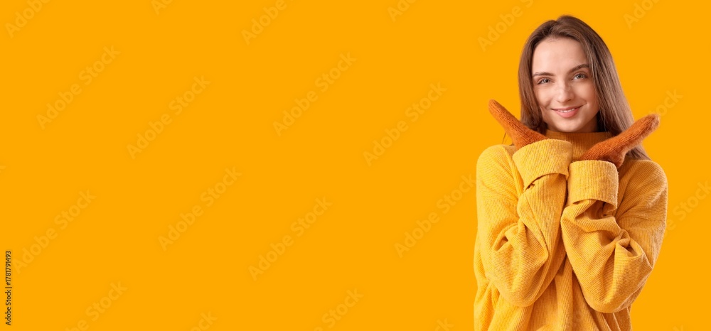 Fototapeta premium Beautiful young woman in stylish sweater and mittens on yellow background with space for text