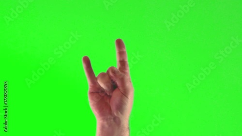 Close-up of a man's hand making rock horns sign against a bright green background
