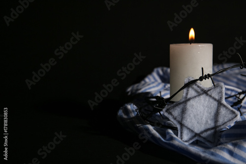 Foto Burning candle with barbed wire, Jewish badge and prisoner uniform on dark background