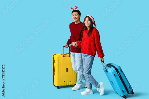 Beautiful young Asian couple with suitcases on blue background. Christmas cel...