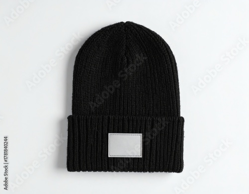 Black knit beanie with label displayed on white background, featuring a blank patch for customizable branding or logo placement, ideal for winter fashion.