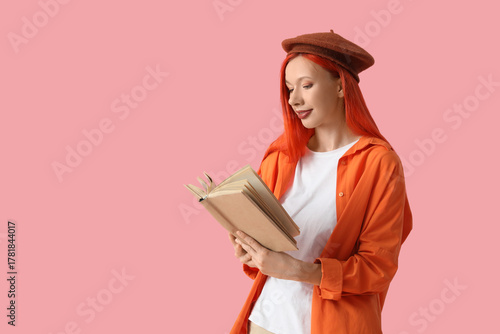 Beautiful young happy woman in beret reading book on pink background