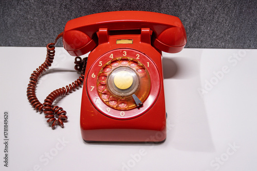 Vintage rotary telephone red retro style. A bright red antique telephone with a gold-tone center dial rests on a white surface, evoking 20th-century communication nostalgia