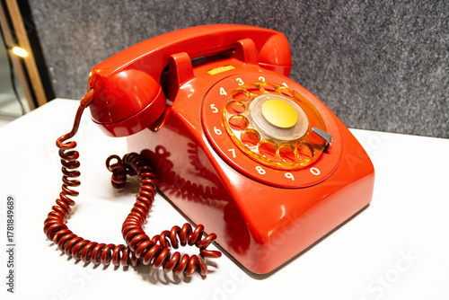 Vintage rotary telephone red retro style. A bright red antique telephone with a gold-tone center dial rests on a white surface, evoking 20th-century communication nostalgia