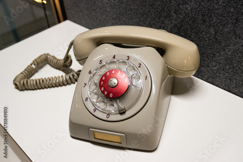 Vintage rotary telephone dial retro classic. A beige grey antique telephone with a red center dial sits on a white surface, representing old technology and communication