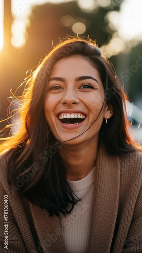 Beautiful young Mexican woman with long dark hair laughs candidly in the warm, golden hour sunlight. Vertical video