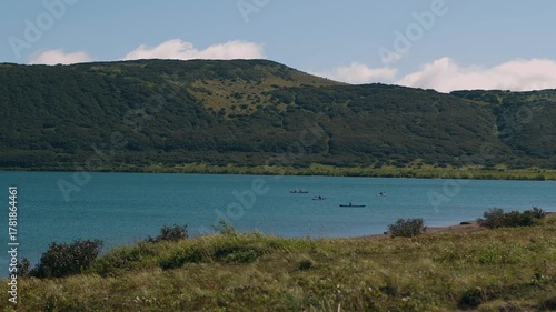 Group of people floats single and double kayaks by steering oars in picturesque bay surrounded by green mountains. Concept is sports and active recreation