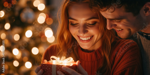 Happy young couple sharing a magical Christmas moment with a glowing gift. Woman smiling while receiving a holiday present