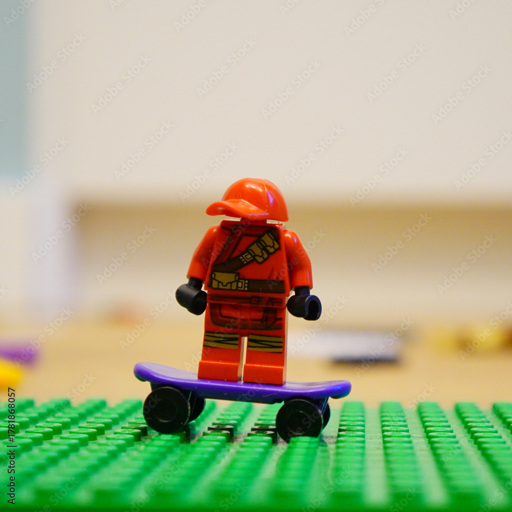 Fototapeta premium Lego minifigure in red riding a purple skateboard on a green baseplate