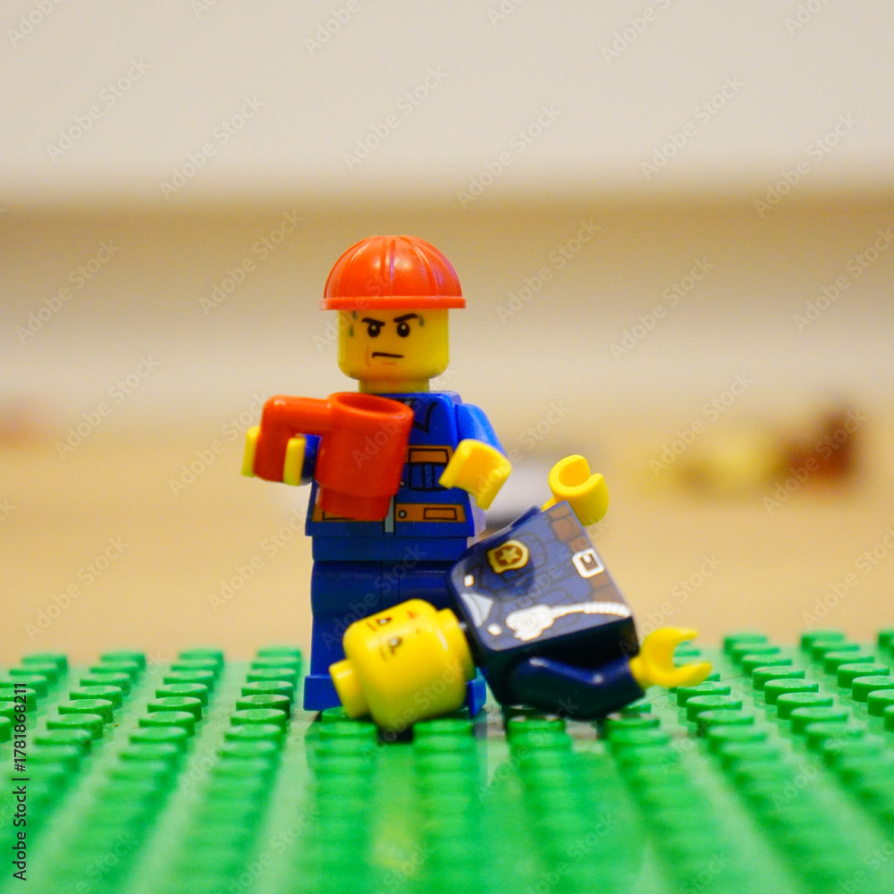 Fototapeta premium Lego construction worker confronts fallen police officer on a green baseplate