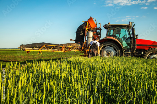 Fototapete Farmer operating agriculture machinery spraying crops on a field