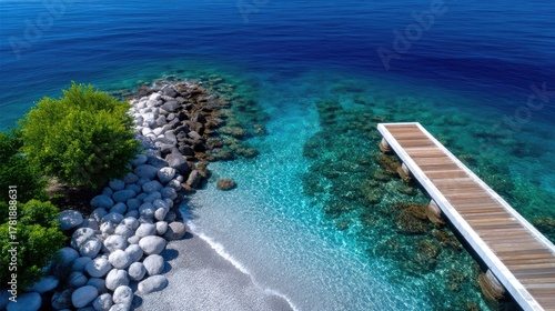 Overhead View Of A Wooden Pier Extending Into Clear Turquoise Water With Lush Green Bushes And Rocky Shoreline
