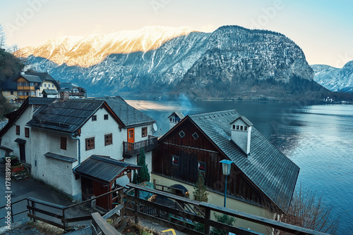 Scenic view of charming lakeside village with traditional houses, surrounded by majestic mountains and serene waters reflecting the sky