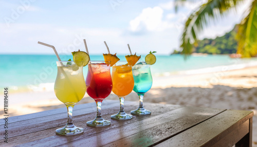 Fototapeta Naklejka Na Ścianę i Meble -  Vibrant yellow, red, orange, and blue cocktails on a wooden surface with a sunny, white sand beach, turquoise ocean, and palm trees as the background.